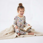 Child in floral pajamas reading a book on a white background