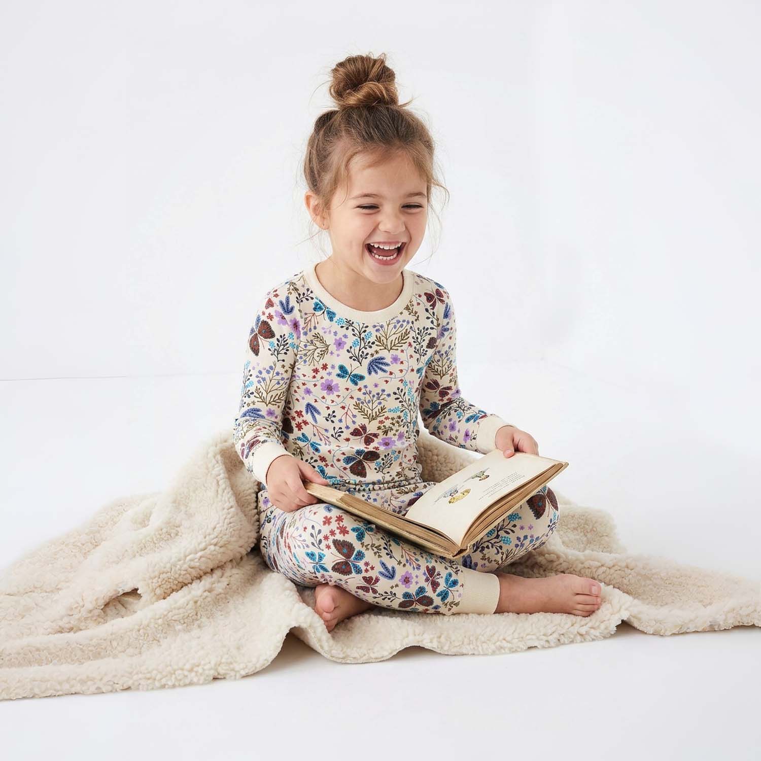 Child in floral pajamas reading a book on a white background