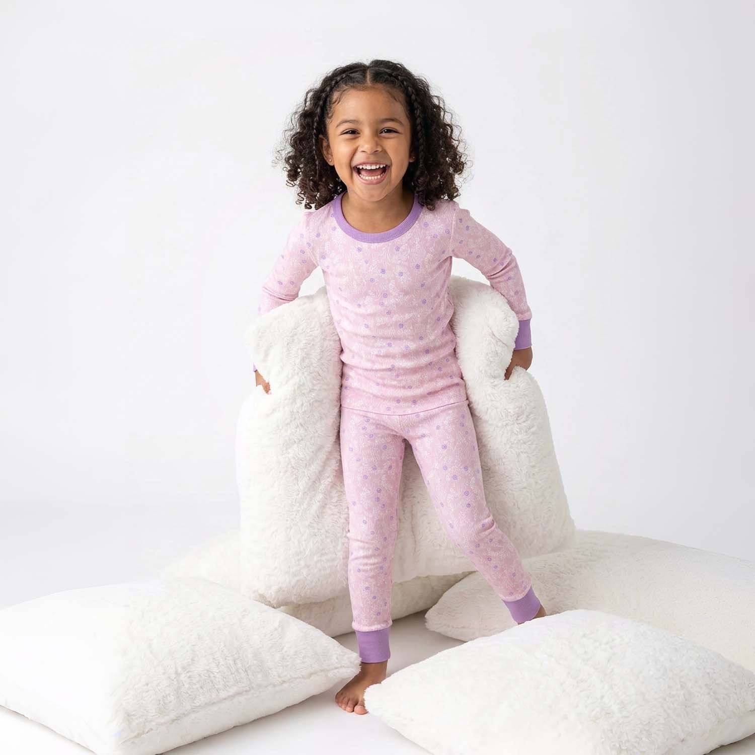 Child wearing pink pajamas with a white pillow background
