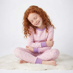 Child wearing pink pajamas with purple cuffs and trim sitting on a white surface.