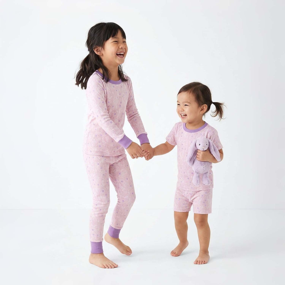 Two children wearing pink pajamas holding hands on a white background