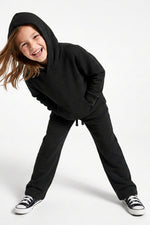 A young girl wearing a matching black hooded sweatshirt and sweatpants set, posing dynamically on a clean white studio background.