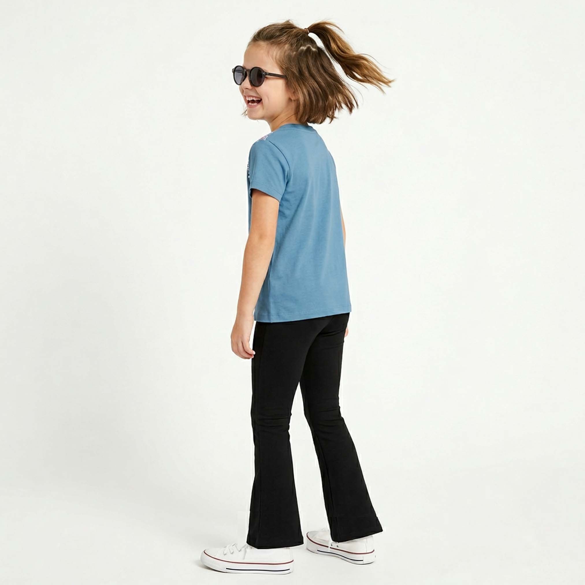 Child wearing a blue t-shirt and black flared yoga pants on a white background