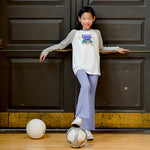girl wearing a rebel girls graphic long sleeve tee shirt and light purple flared yoga pants with a soccer ball standing against a door