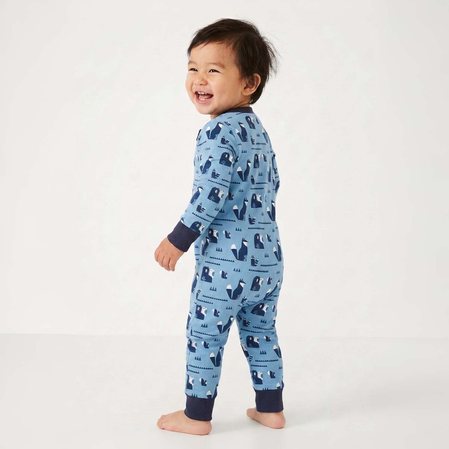 Baby standing wearing a blue pajama with animal pattern on a white background