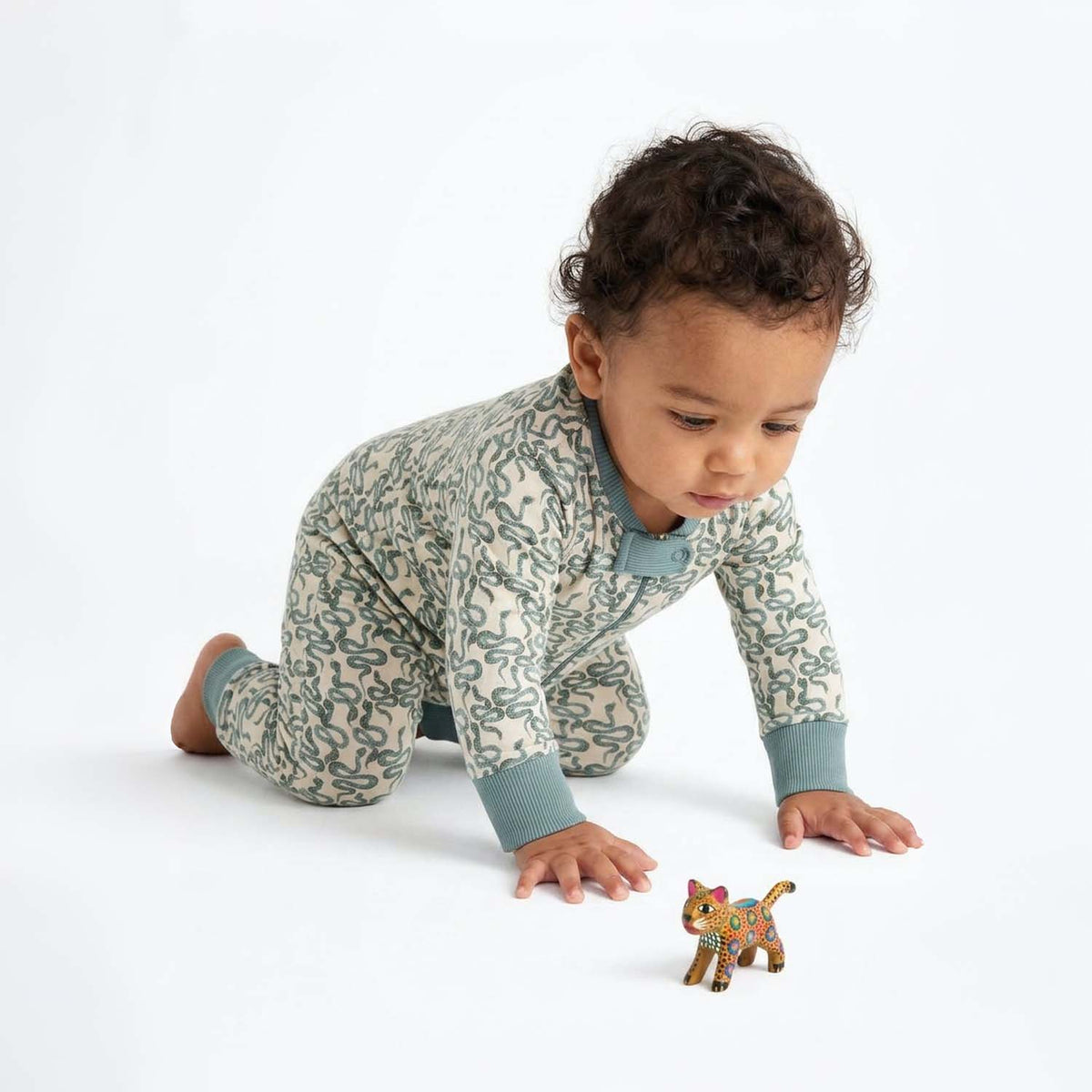 Baby crawling wearing pajamas with green snakes on a white background