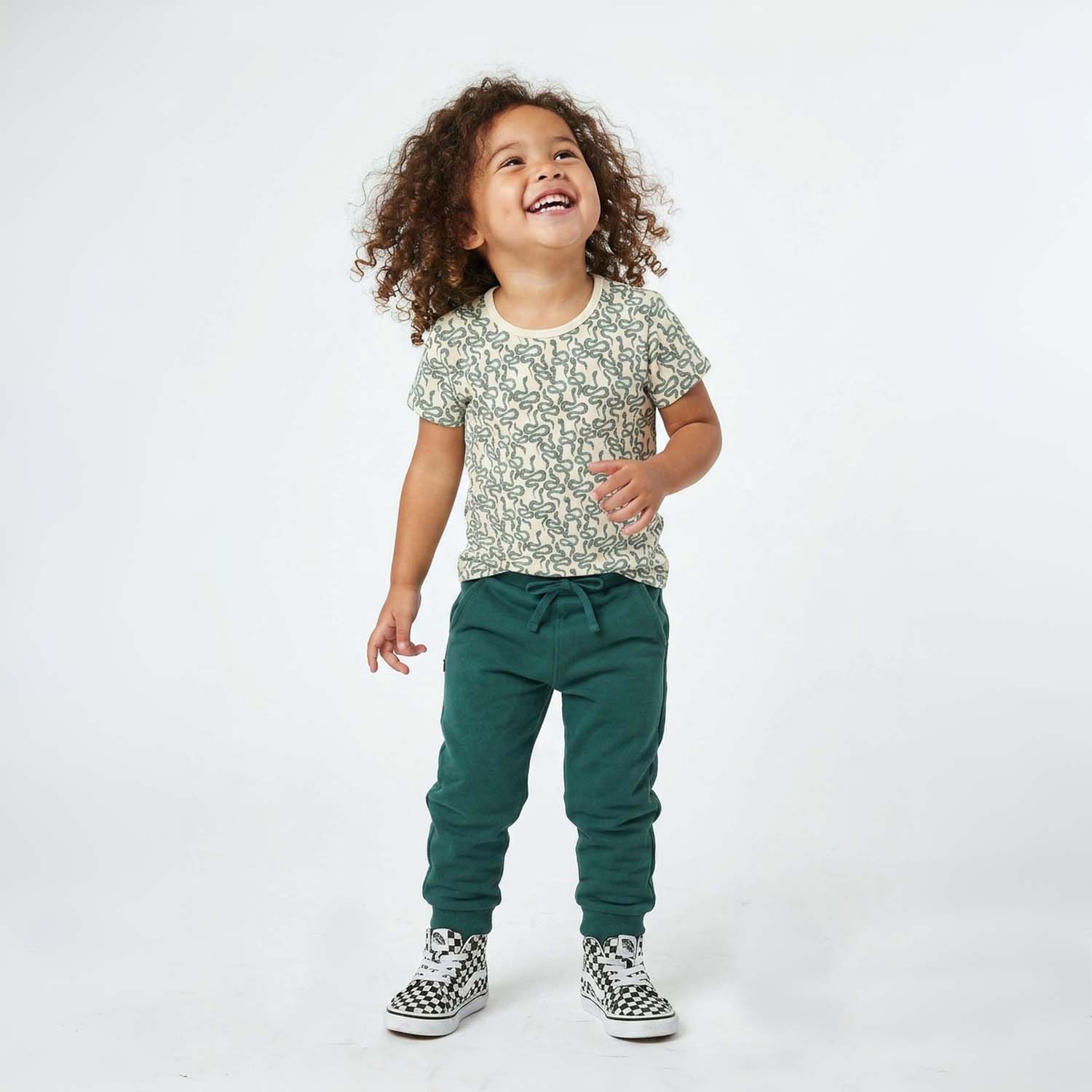 Child wearing a snake patterned shirt and green pants on a white background