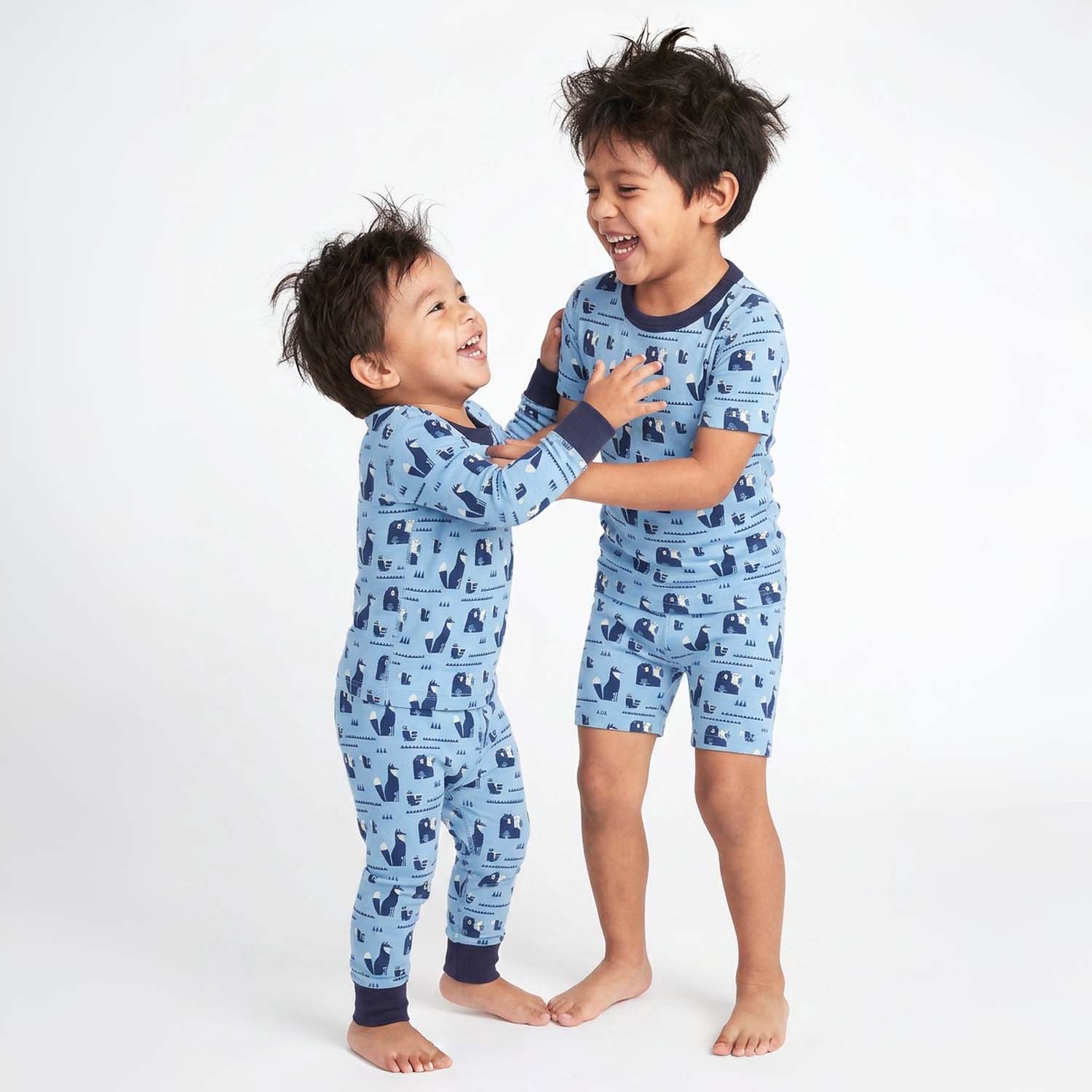 Two children wearing blue pajamas with a pattern, standing on a white background
