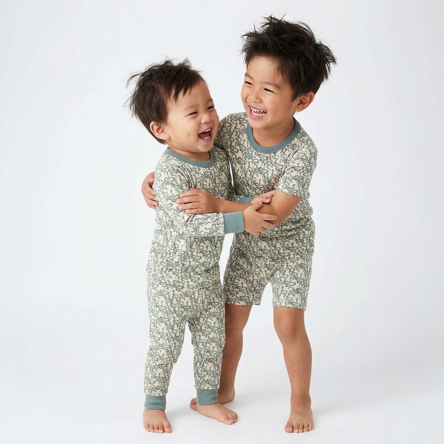 Two children wearing matching green snake pattern pajamas on a white background