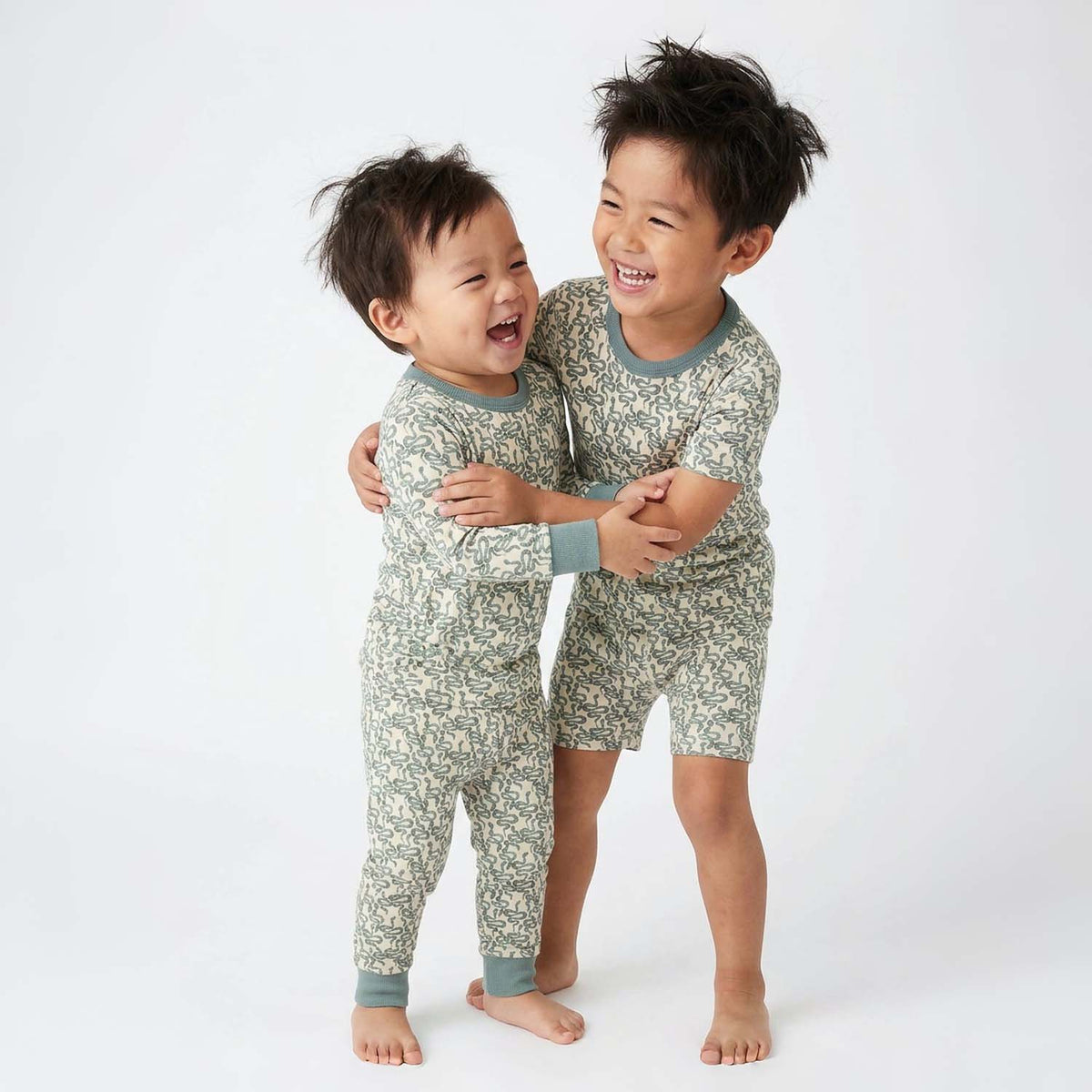 Two children wearing matching green snake pajamas on a white background