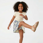 Young girl wearing a floral skirt with built-in short and ivory shirt on a white background