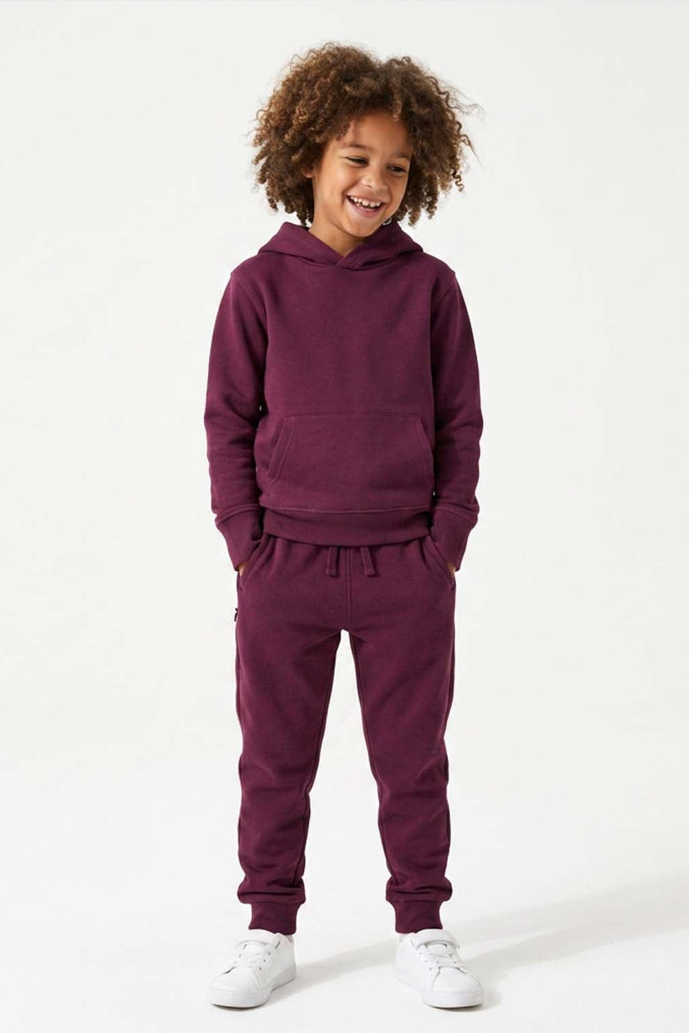 A young child with curly brown hair wearing a matching deep purple hoodie and jogger sweatpants set, standing against a clean white studio background.