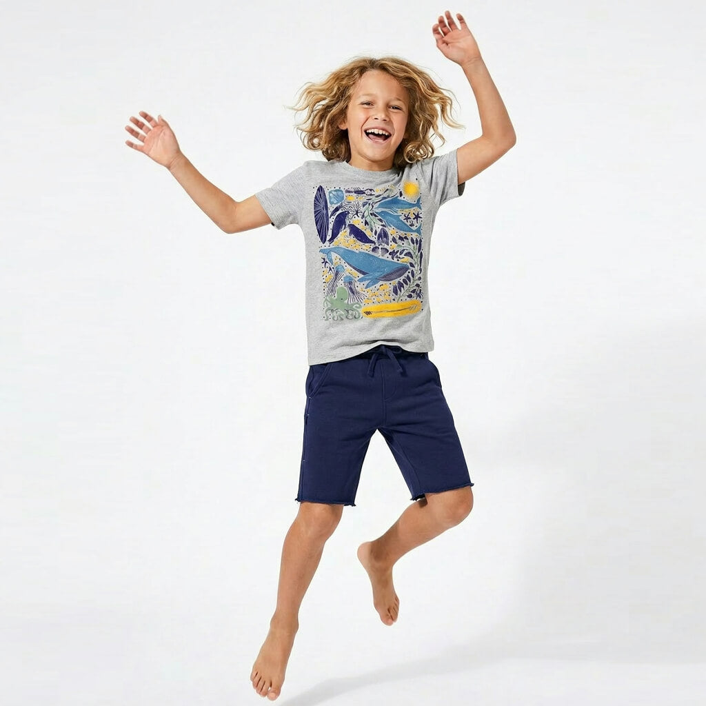 Child wearing a gray t-shirt with a colorful design and navy shorts, jumping on a white background