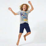 Child wearing a gray t-shirt with a colorful design and navy shorts, jumping on a white background