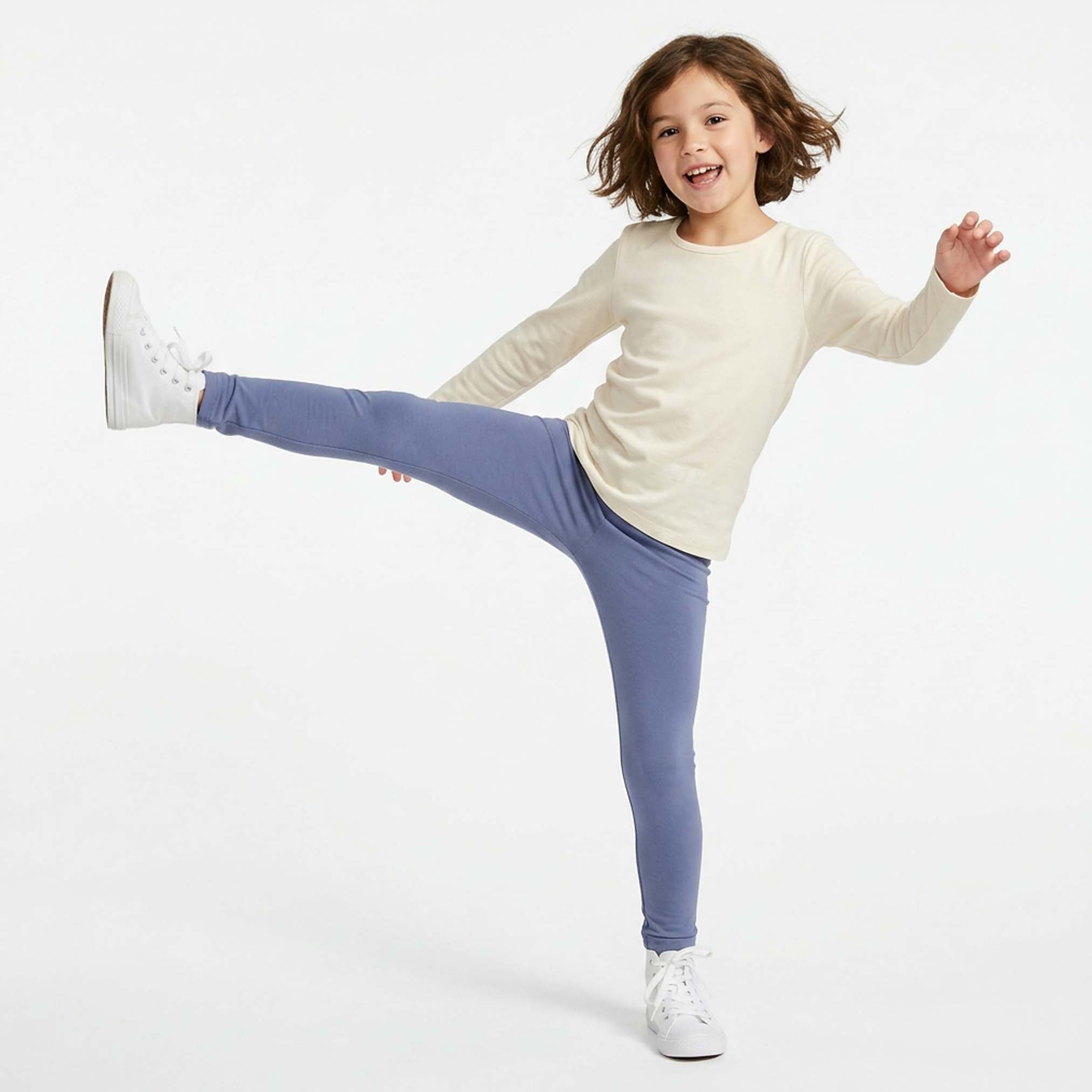 Child wearing a white long-sleeve shirt and purple leggings on a white background
