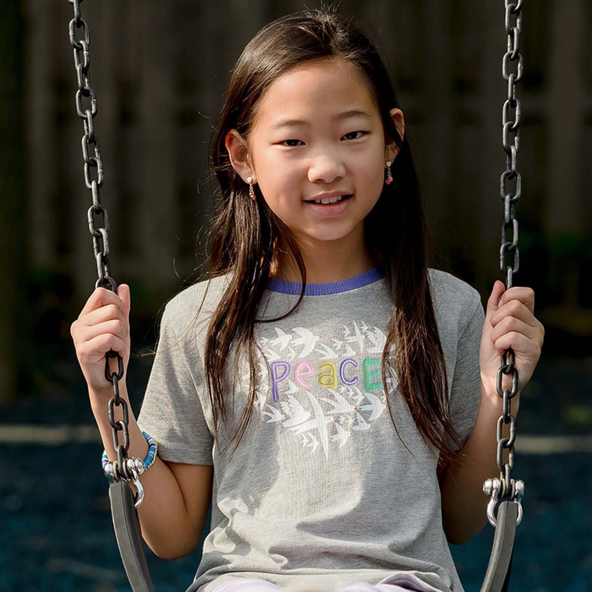 Young girl sitting on a swing wearing a t-shirt with 'Peace' printed on it.