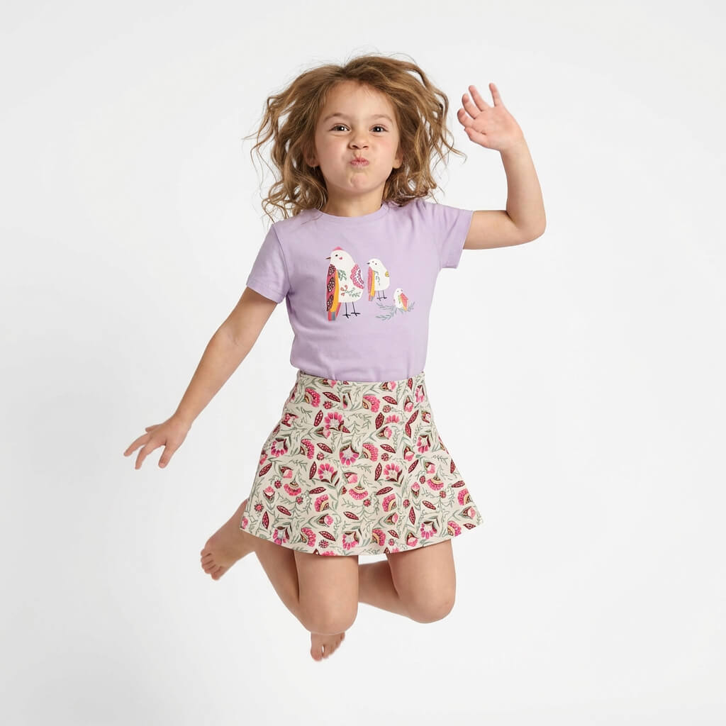 Child wearing a purple t-shirt with a colorful design and a floral skirt on a white background