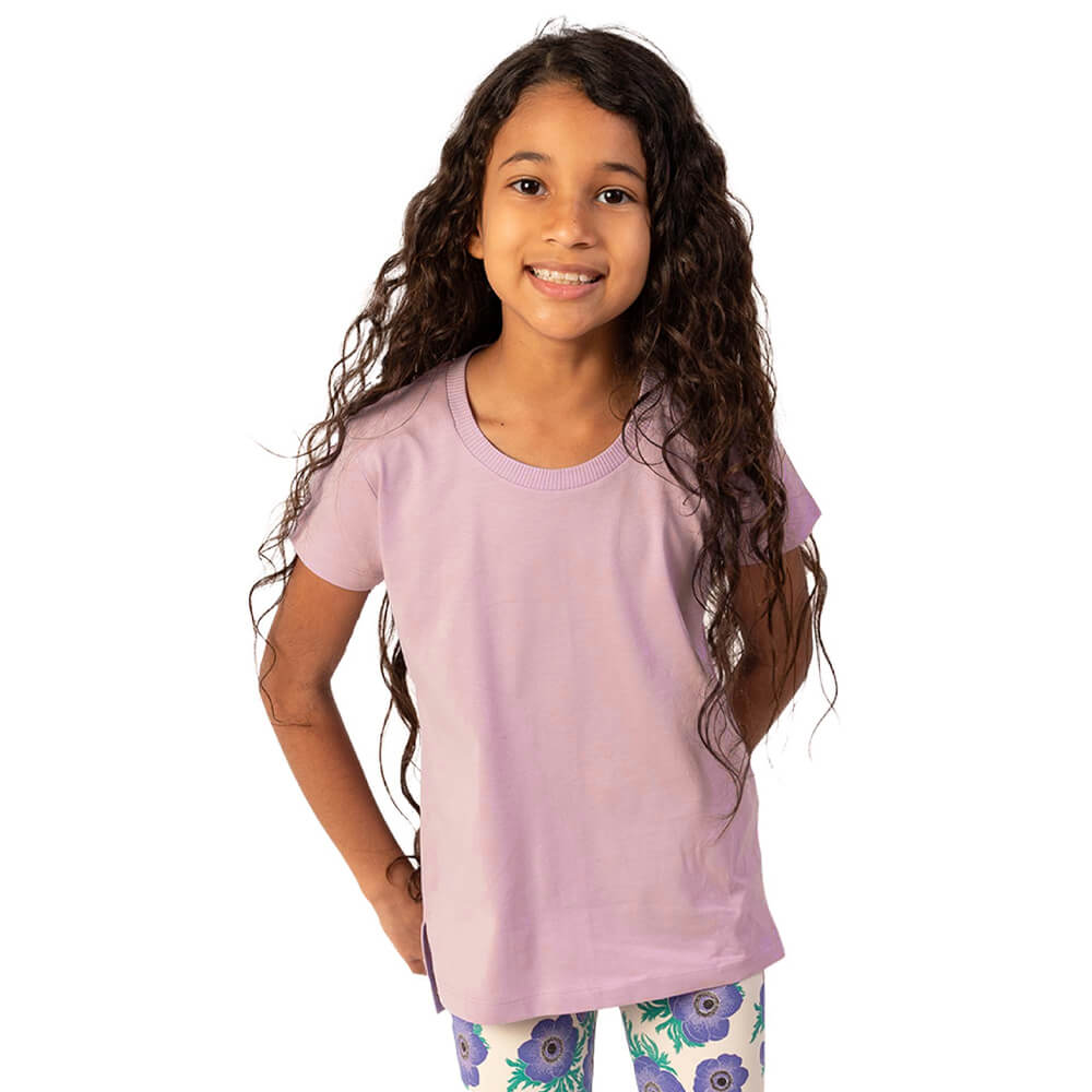Young girl wearing a light purple t-shirt and patterned leggings on a white background