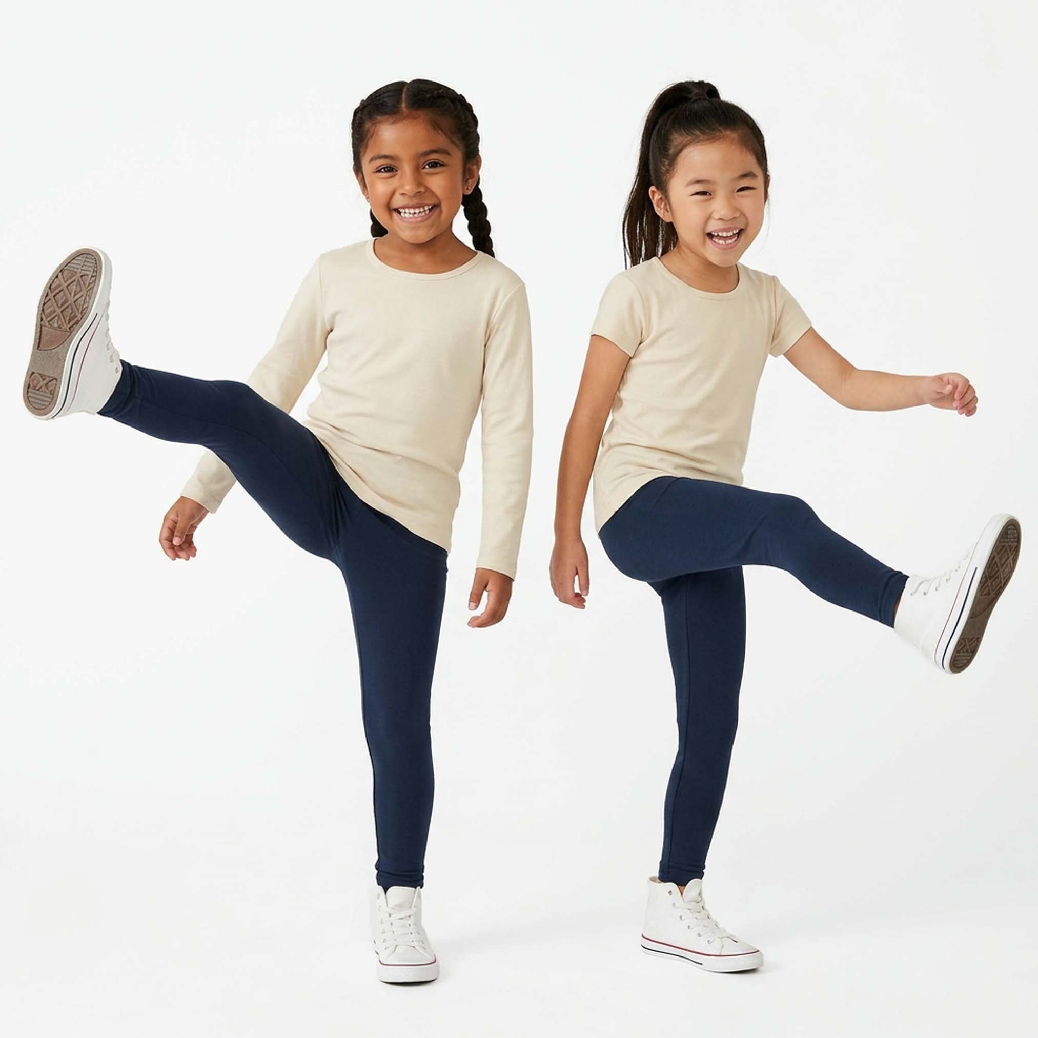 Two young girls wearing navy leggings and cream tops on a white background