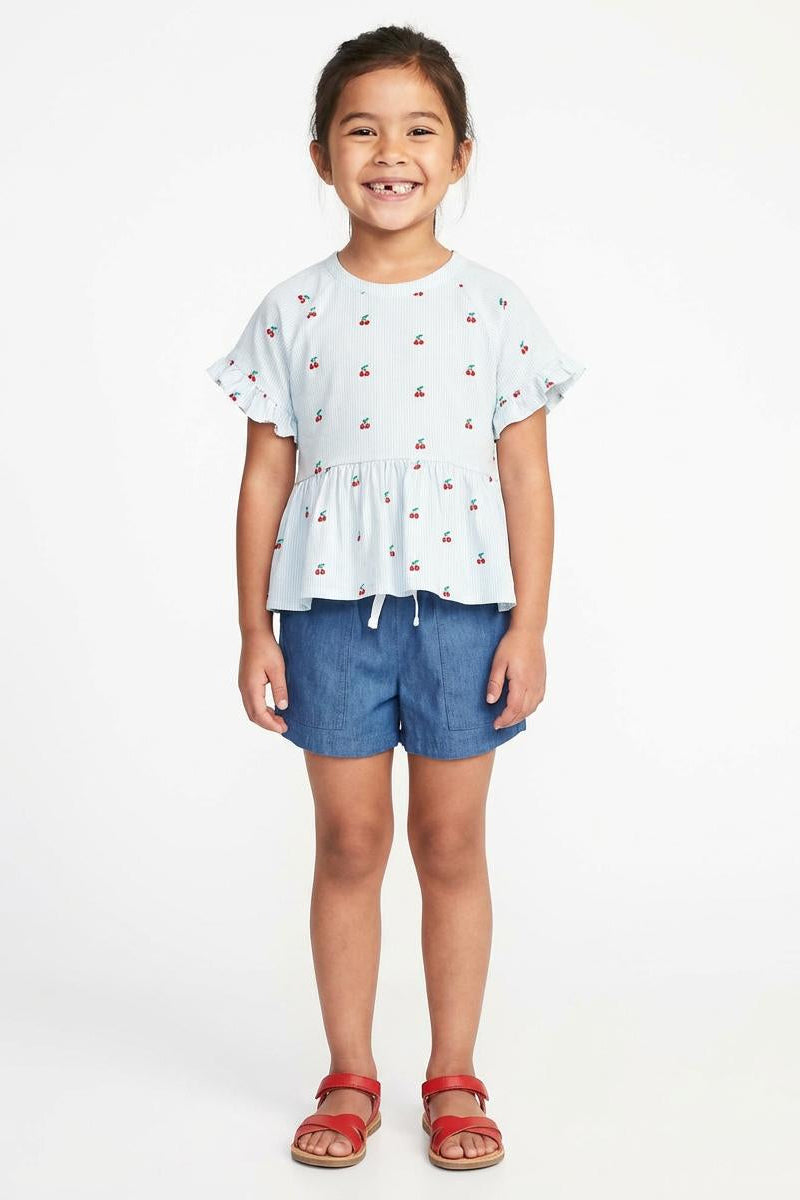 Young girl wearing a white top with small patterns and blue shorts on a white background