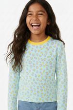 Young girl wearing a light blue long-sleeve shirt with a floral pattern on a white background
