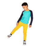a boy in an active pose wearing a navy and teal long sleeve baseball tee and yellow sweatpants 
