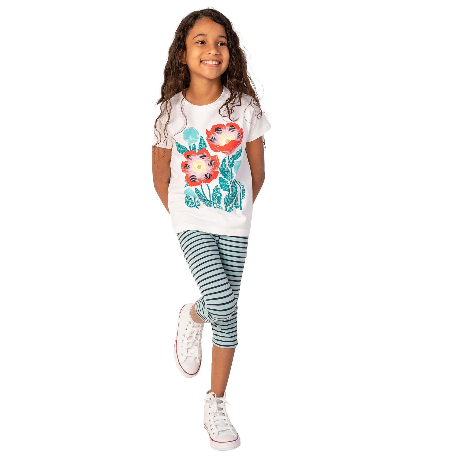 A girl wearing a white shirt with a floral print and striped leggings on a white background