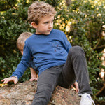 a young boy sitting on a rock wearing a blue long sleeve tee with a galaxy print on the pocket