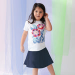 girl wearing a white tee shirt with a floral print and a navy blue skirt against a pastel background