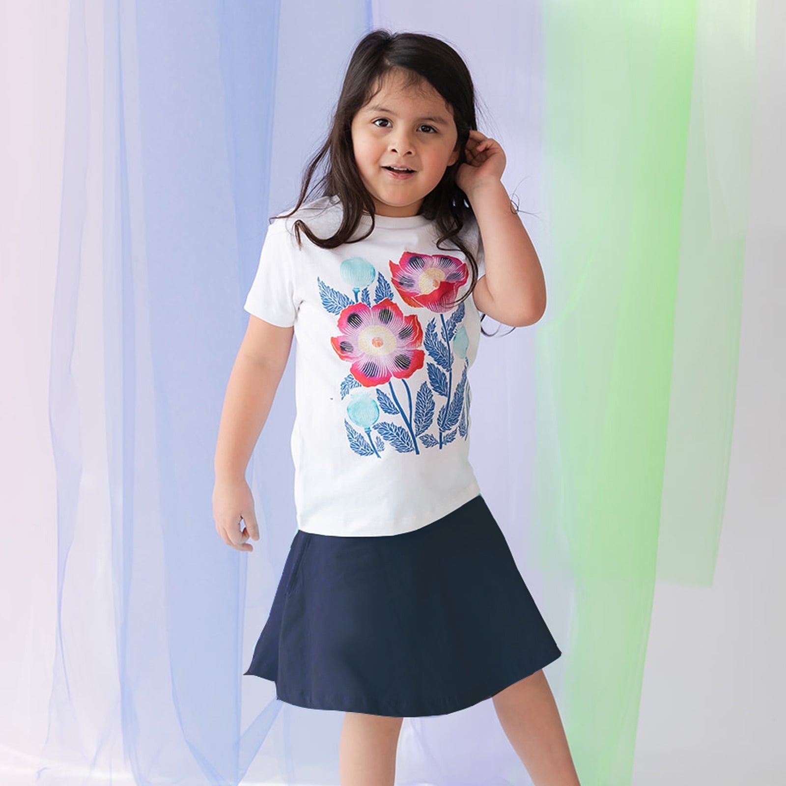 girl wearing a white tee shirt with a floral print and a navy blue skirt against a pastel background
