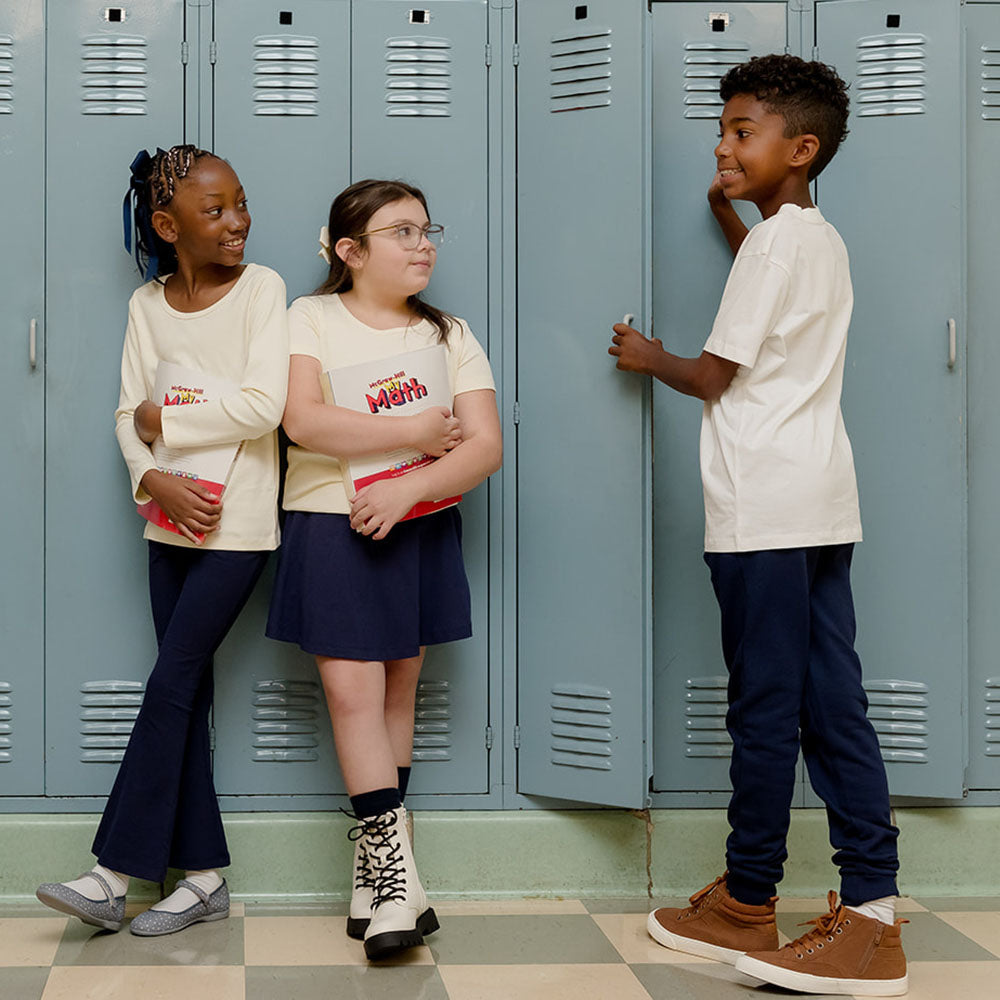 three kids standing against school lockers all are wearing navy blue bottoms and white tops