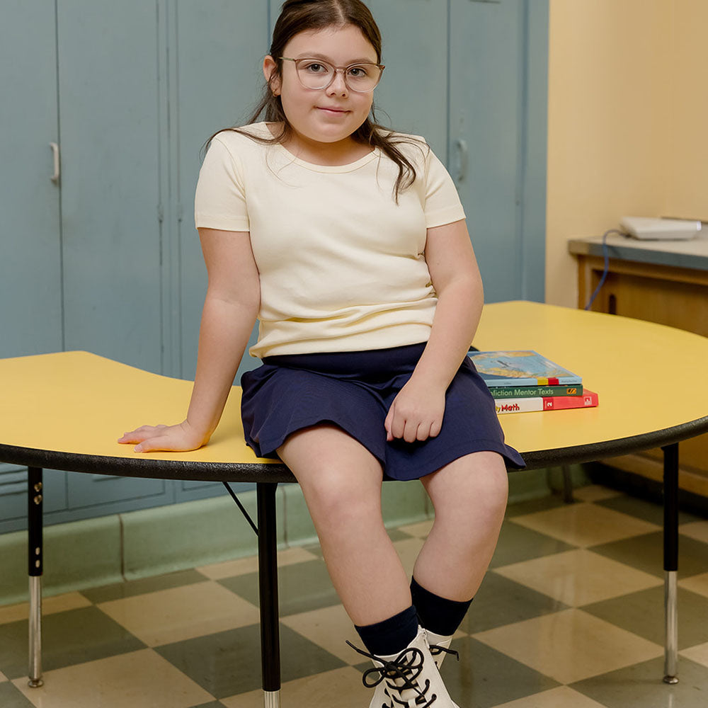 girl sitting on a desk wearing an ivory tee shirt and navy skirt