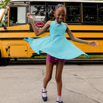 A girl twirling in a sleeveless turquoise dress and pink shorts with a school bus in the background
